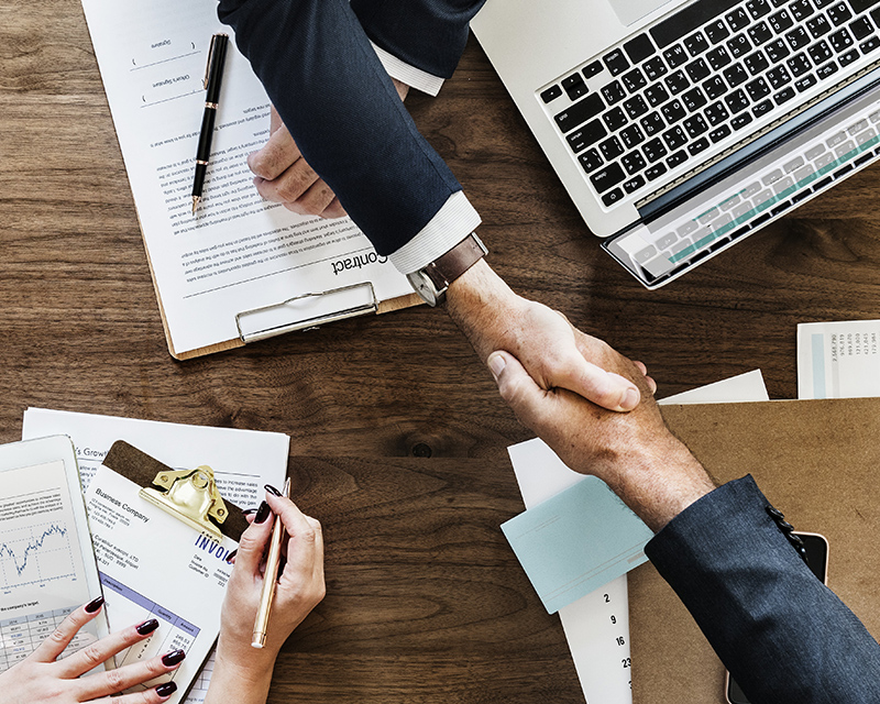 Businessmen shake hands across the table with laptop and notes laid out